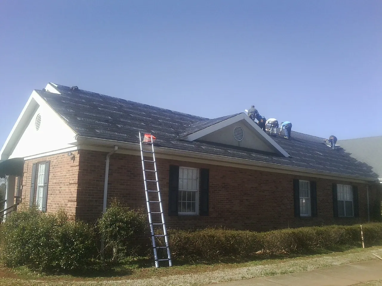 Crew tearing shingles off a brick ranch roof with a ladder set — Emergency Roof Repair work by our crew in Tangent