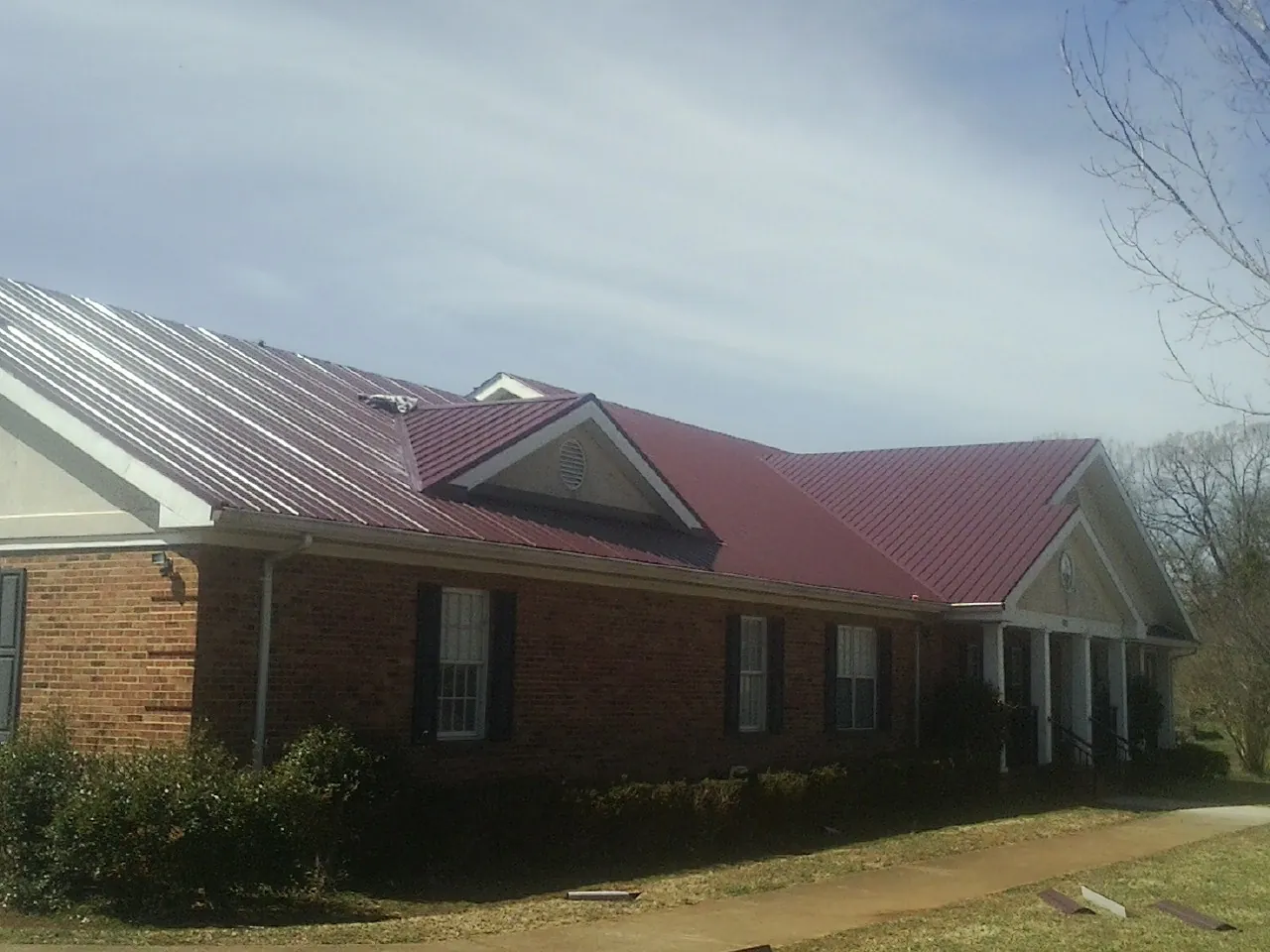 Red metal roof with gabled entries on a long brick building, from a Hail Damage Roof Repair job in Tangent