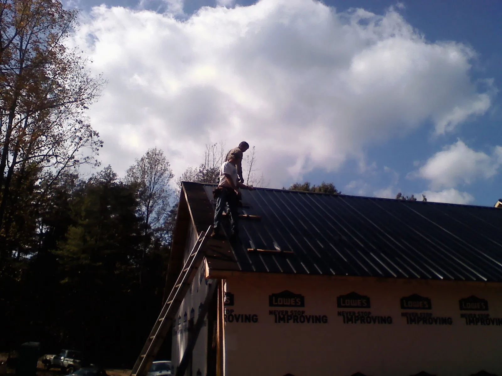 Roofer fastening dark metal panels high against a cloudy sky, from a Roof Inspection job in Tangent